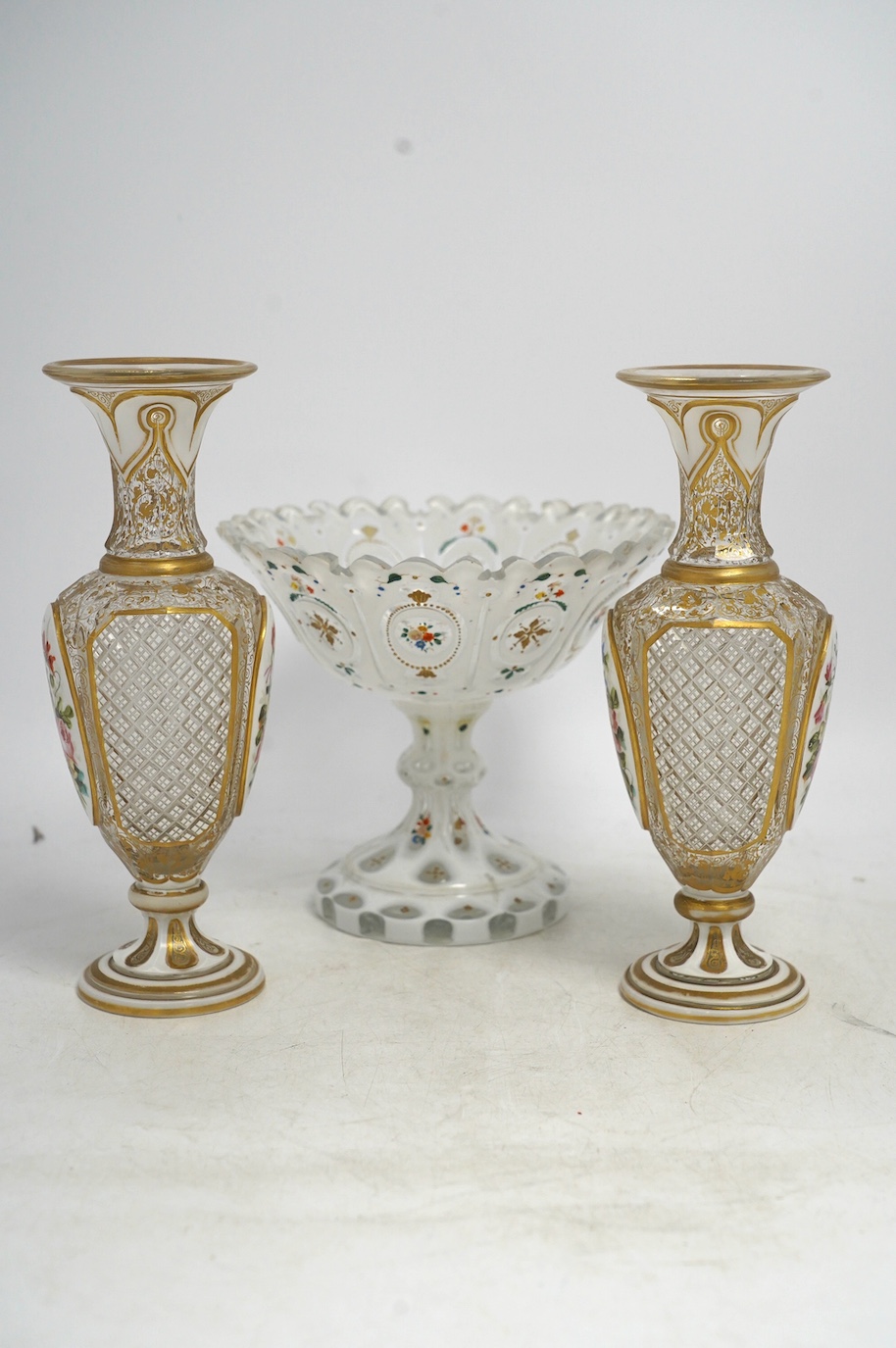 A pair of late 19th century Bohemian enamelled overlaid glass vases, and a similar overlaid glass comport. Condition - vases fair; comport poor